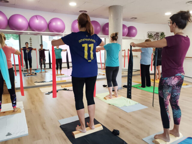 Grup de persones dempeus fent exercicis amb bandes elàstiques i suports de fusta.