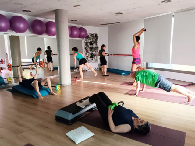 Participants fent exercicis de tonificació amb pesos i matalassos en una sala.