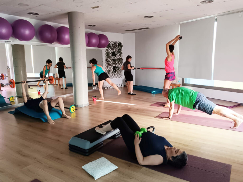 Sessió de tonificació amb pesos. Participants fent exercicis de tonificació amb pesos i matalassos en una sala.