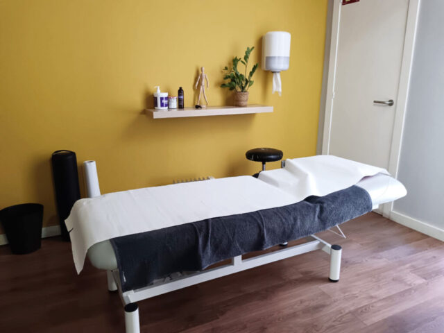 Llitera preparada en una sala de fisioteràpia amb paret groga i prestatgeria.