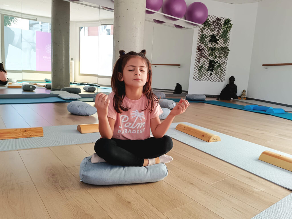Meditació en sala de ioga. Persona jove asseguda en un coixí meditant en una sala de ioga.