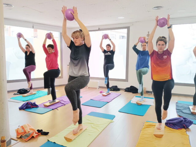 Participants en equilibri sobre taulons aixecant pilotes petites per sobre del cap.