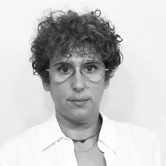 Retrat en blanc i negre de Sandra Rodríguez amb cabell curt i arrissat i ulleres, portant camisa clara i jersei.