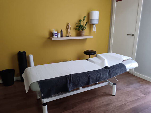 Llitera blanca amb tovallola fosca en una sala de tractament amb paret groga.